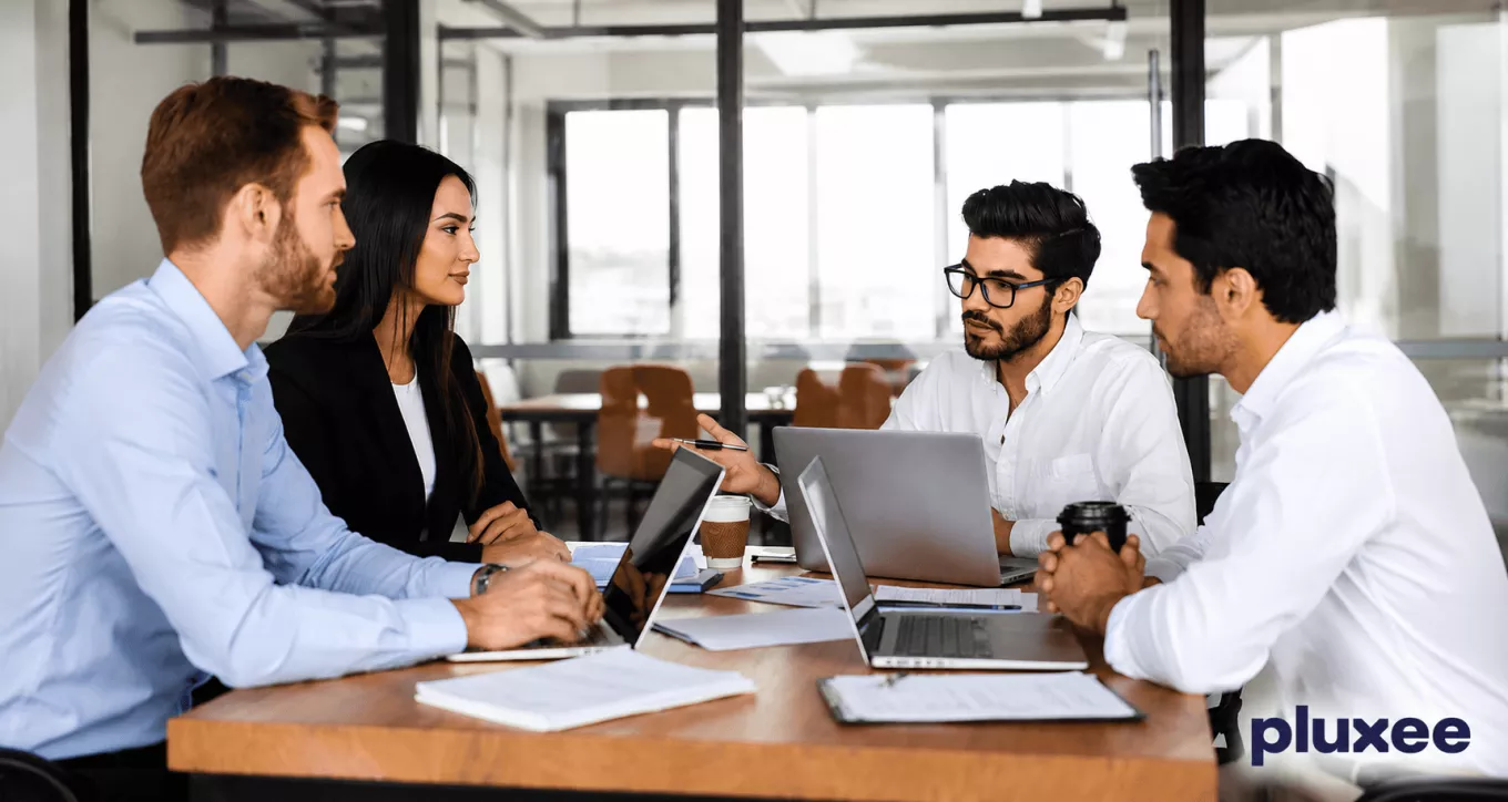 Equipo de trabajo colaborando en una mesa de oficina con computadoras portátiles, representando el liderazgo y el trabajo en equipo.
