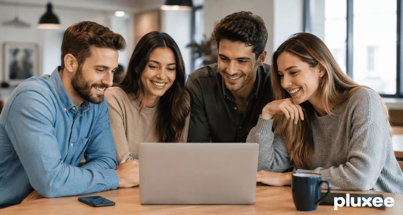 Un equipo de trabajo sonriente y colaborativo reunido alrededor de una computadora portátil en una oficina, demostrando compromiso laboral.