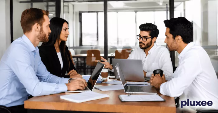 Equipo de trabajo colaborando en una mesa de oficina con computadoras portátiles, representando el liderazgo y el trabajo en equipo.