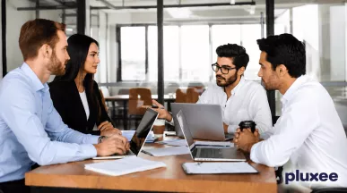 Equipo de trabajo colaborando en una mesa de oficina con computadoras portátiles, representando el liderazgo y el trabajo en equipo.